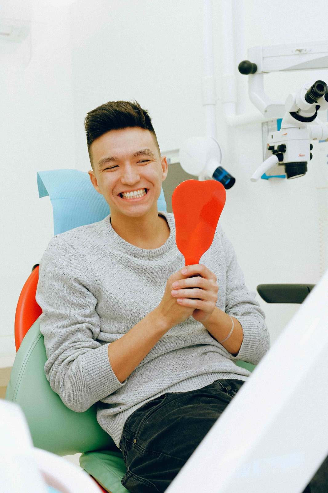 Smiling young man in a dental chair, holding a red dental impression tray and looking delighted.